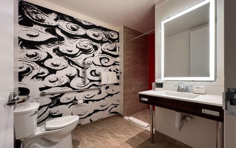 A modern bathroom with a toilet, sink, and shower, featuring a striking black and white wall art