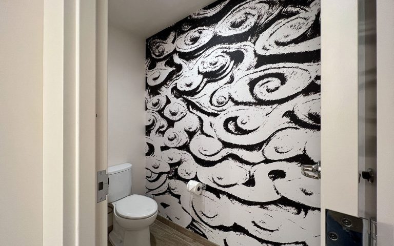 A bathroom with a toilet and a unique black and white wallpaper.