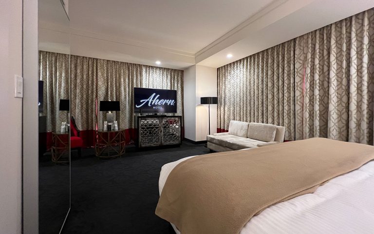 A wide view of a hotel room with a bed, sofa, TV, and mirror