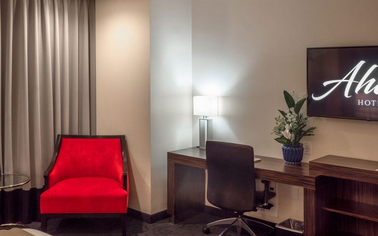 A hotel room with a red chair, desk, and TV.