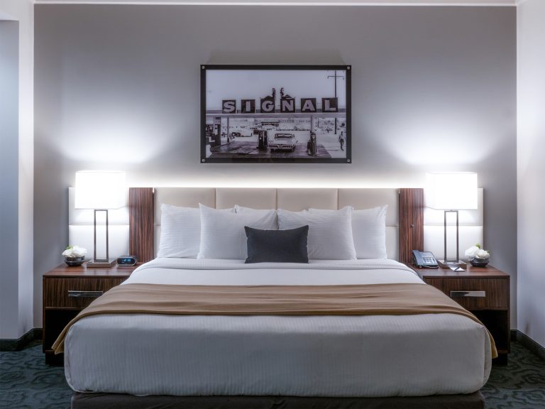 A neatly made king-sized bed with white bedding, a brown throw blanket, and a framed picture above the headboard.