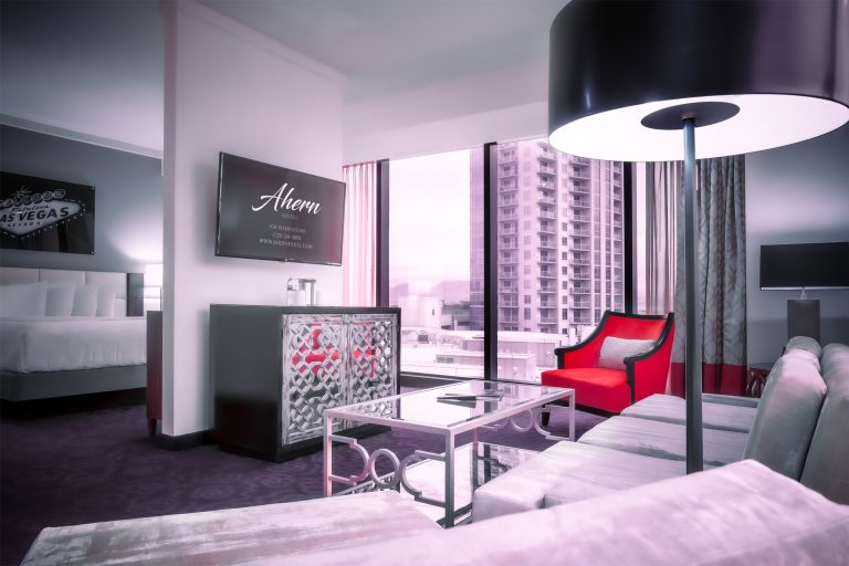 A luxurious hotel room with a large window, city view, red accent chair, and modern furniture.