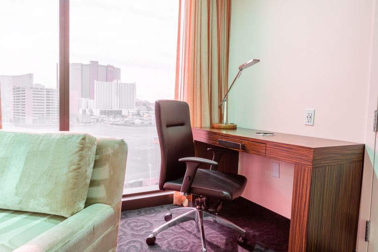 A hotel room with a desk, chair, sofa, and city view.