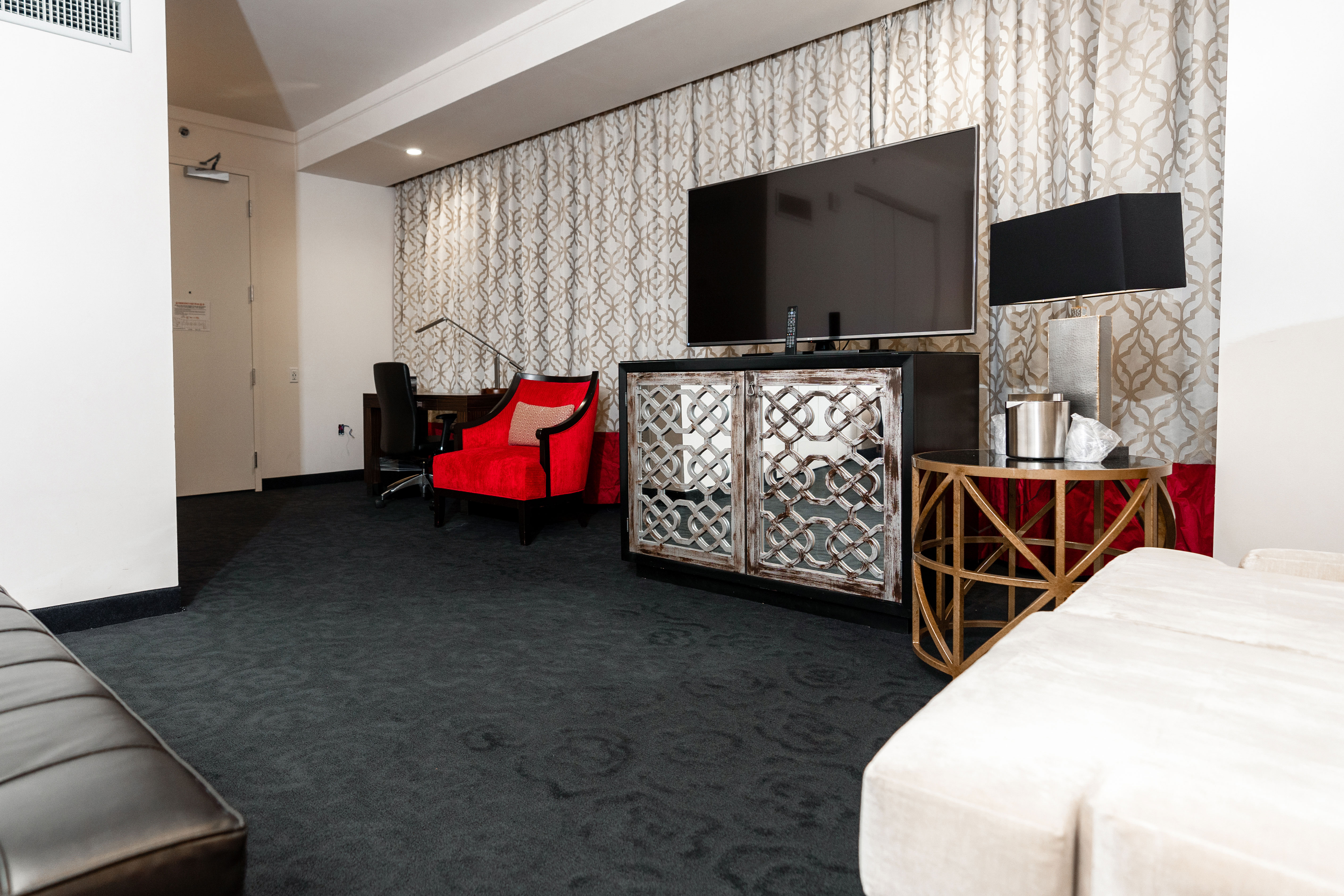 A wide view of a hotel room with a red chair, desk, TV, and bed.