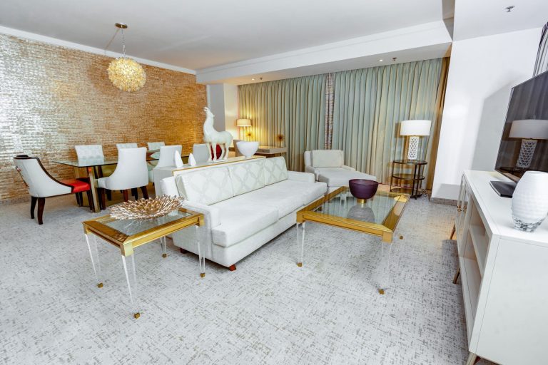 A wide view of a luxurious living room with a dining area, white furniture, and gold accents.